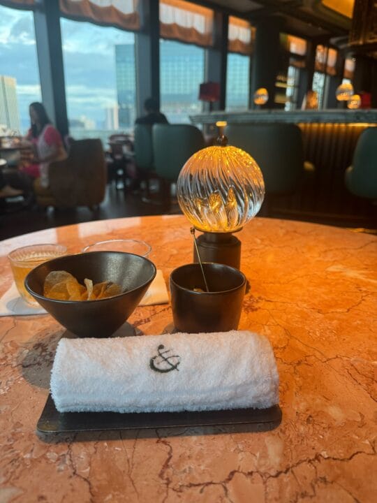 Canes & Talesのテーブル。金色の「&」が入ったおしぼりと、窓の外にはまだ明るい大阪の街