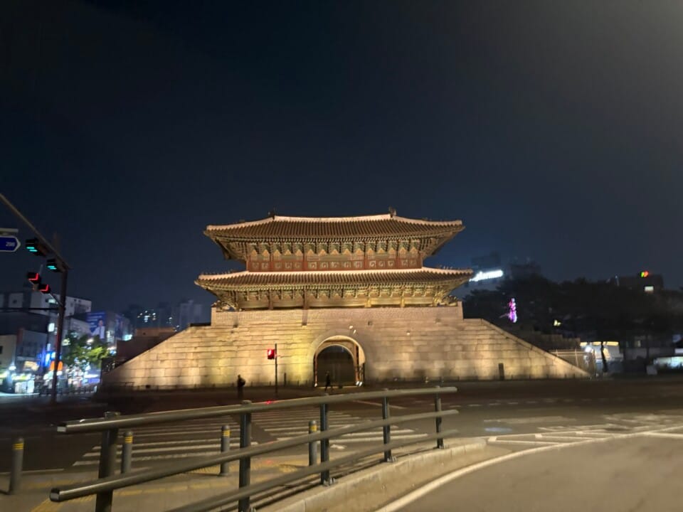 Night view of Namdaemun (Sungnyemun) Gate in Seoul: a lit historic stone base with a two-tier wooden pavilion, at street level with traffic nearby.