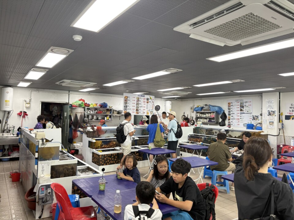 海女の販売場の店内。生簀と青いテーブルが並び、家族連れで賑わう