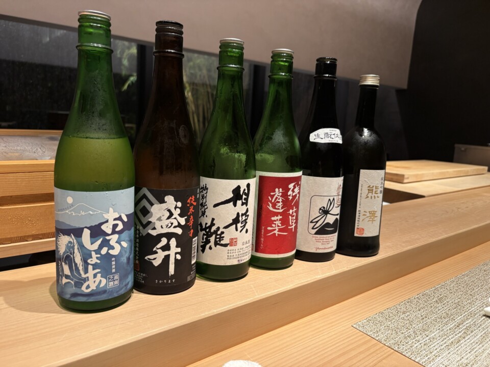 Six bottles of Kanagawa local sake lined up on the sushi counter
