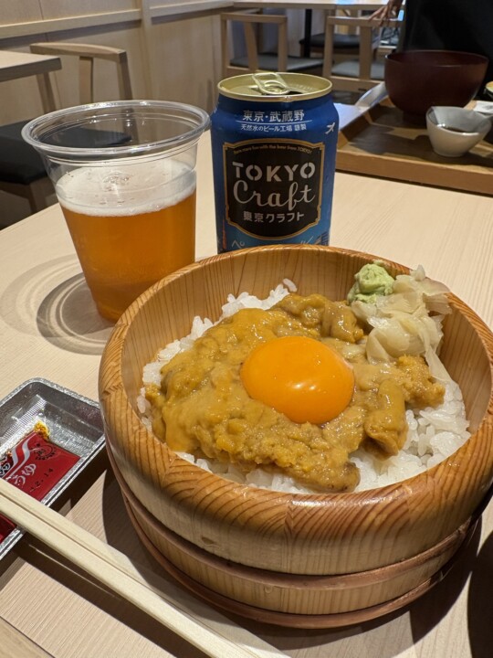 木桶に盛られたうに丼。中央に卵黄がのり、東京クラフトの缶ビールが横に置かれている