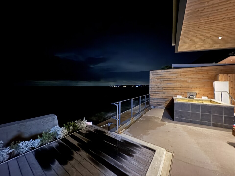 夜のテラス。暗い海と、照明に照らされたグリルと流し台