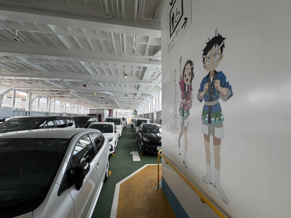 フェリーの車両甲板に並ぶ車と、壁に描かれた「からかい上手の高木さん」のイラスト