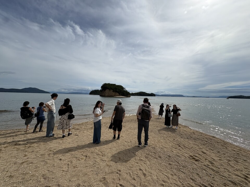 波打ち際に立ち、海に沈んだ道の先の島を眺める人たち
