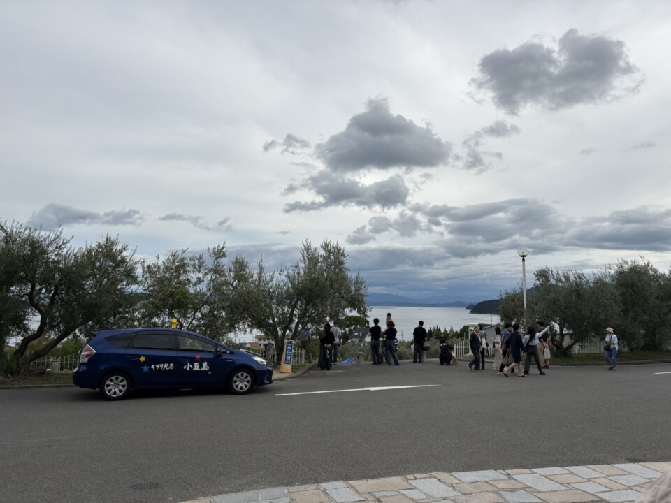 オリーブの木の向こうに広がる瀬戸内海と、園内を歩く人たち